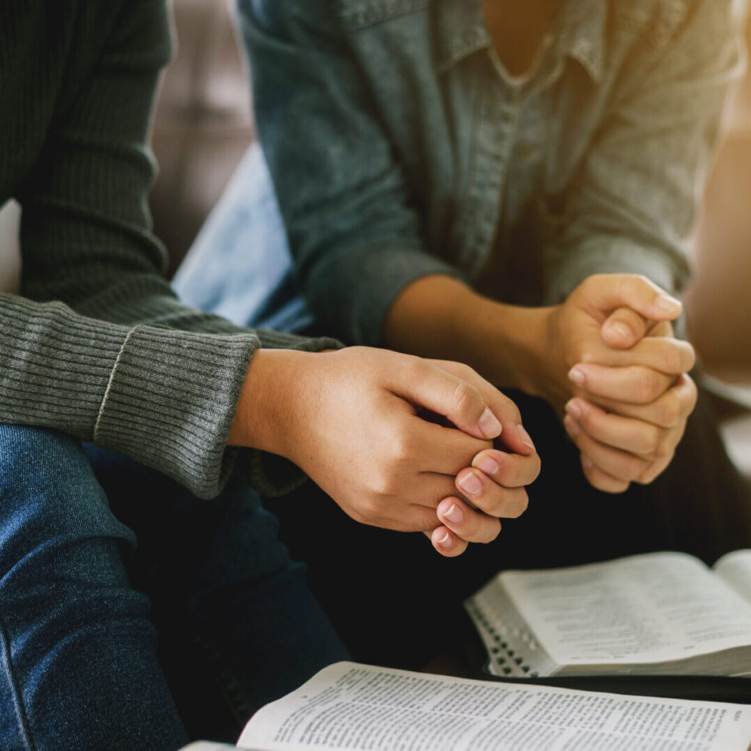 two women reading and study bible in home and pray together. Two people praying with clasped hands.
